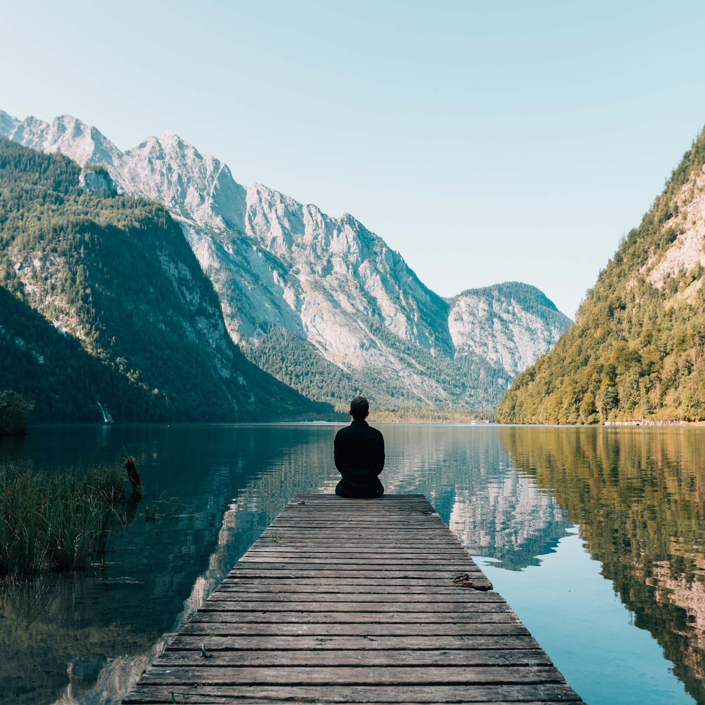 Person sitting on a dock near a lake surrounded by mountains