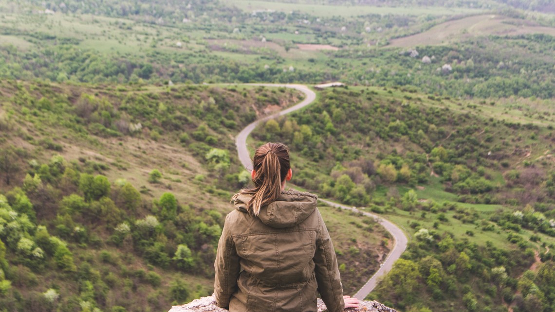 Young woman sits on ledge looking at path