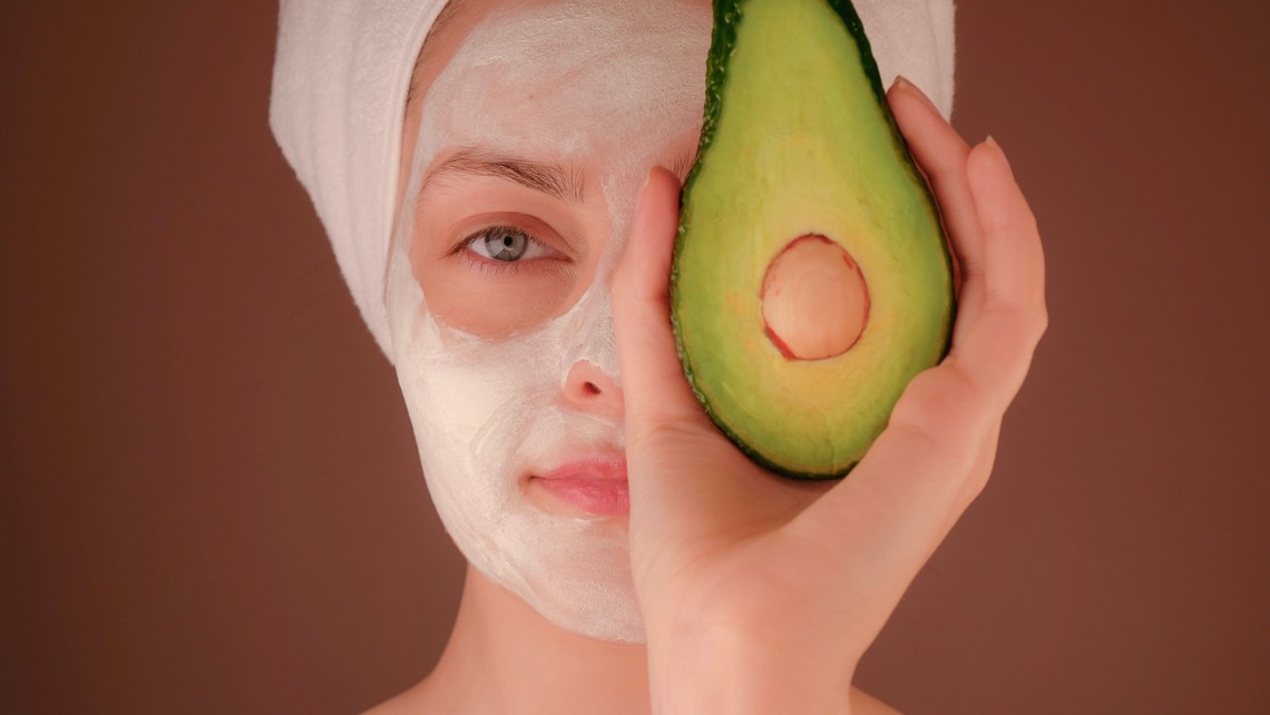 woman with a facial holding an avocado