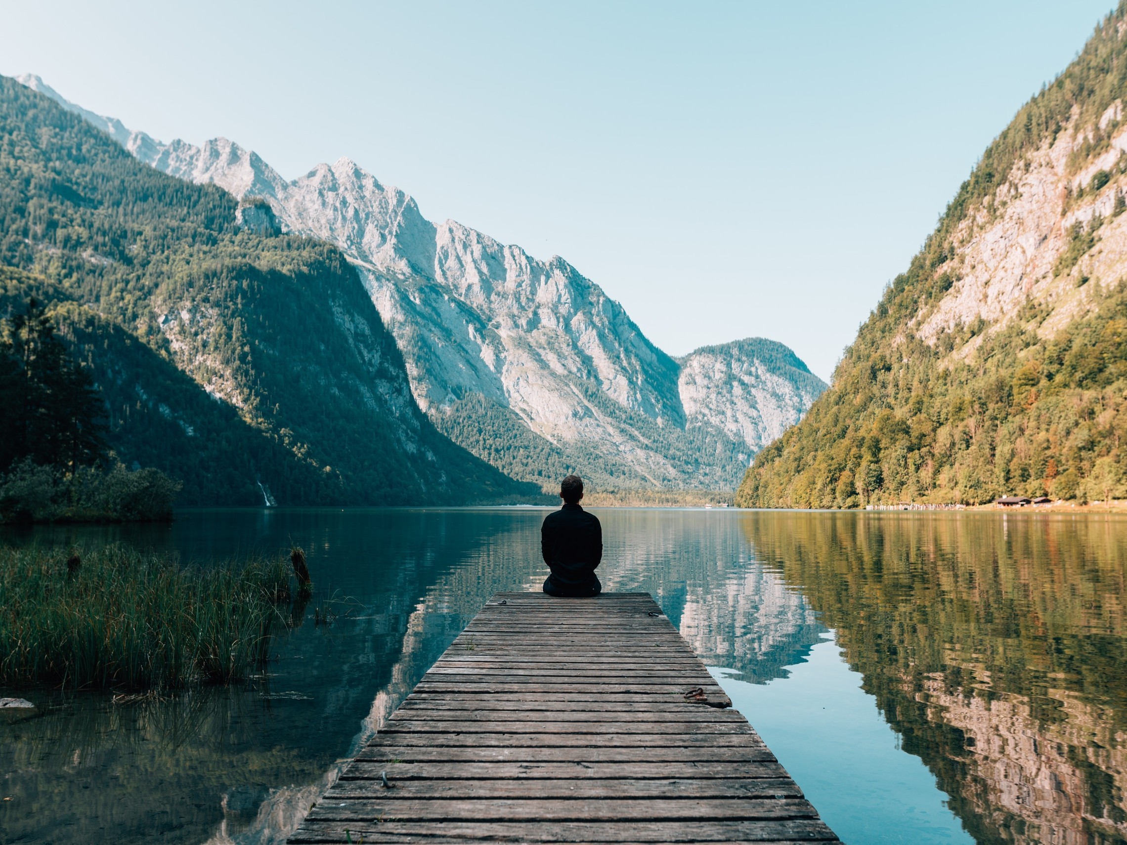 Person sitting on a dock near a lake surrounded by mountains